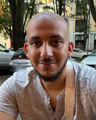 Hanna Filoupatir, souriant, attablé en terrasse dans une rue arborée
